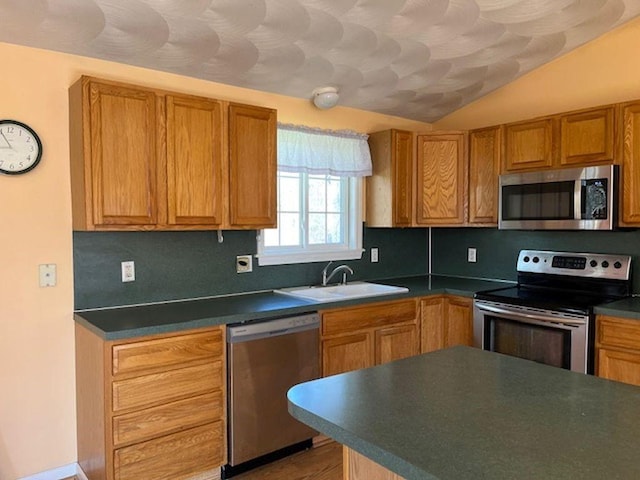 kitchen with dark countertops, vaulted ceiling, appliances with stainless steel finishes, and a sink