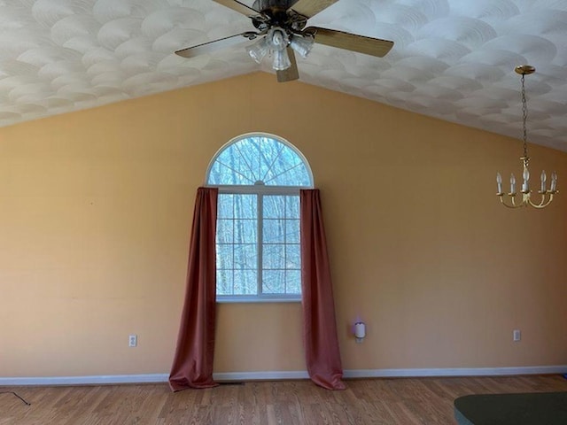 spare room featuring ceiling fan with notable chandelier, baseboards, vaulted ceiling, and wood finished floors