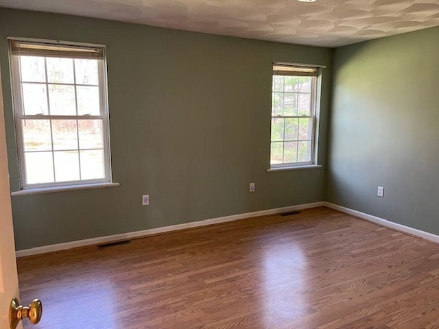 empty room featuring visible vents, baseboards, and wood finished floors