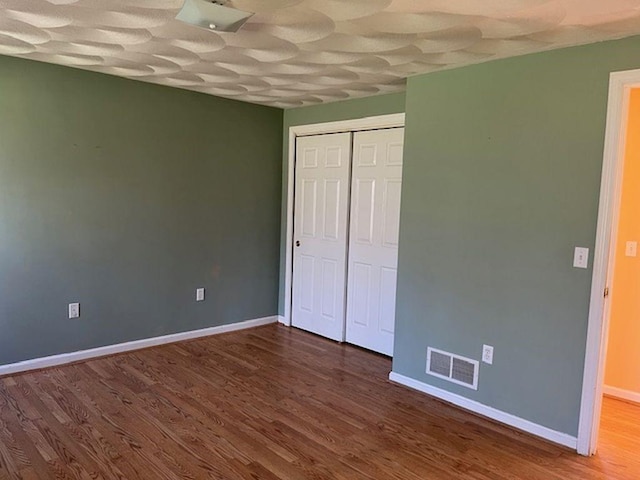 unfurnished bedroom with baseboards, wood finished floors, visible vents, and a closet