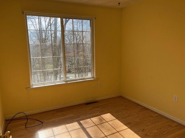 empty room with baseboards, wood finished floors, visible vents, and plenty of natural light