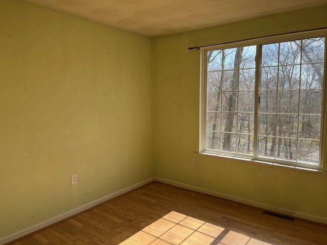 empty room with wood finished floors, visible vents, baseboards, and a healthy amount of sunlight