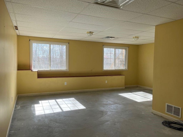 unfurnished room featuring unfinished concrete flooring, baseboards, visible vents, and a paneled ceiling