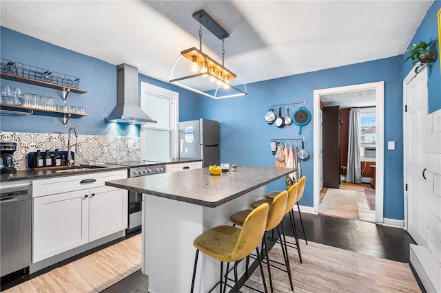 134 Courtland St, Providence, RI 02909 - kitchen with stainless steel appliances, a sink, wall chimney range hood, dark countertops, and wood finished floors