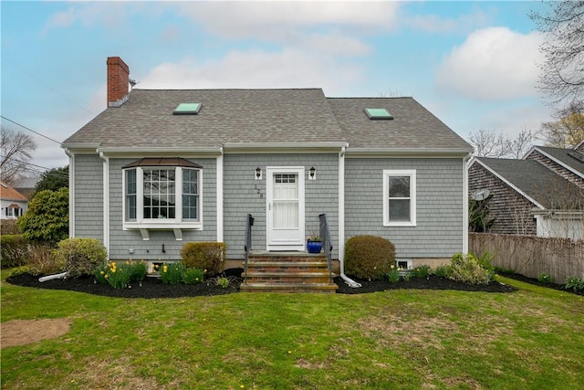rear view of house featuring a chimney, roof with shingles, fence, and a yard