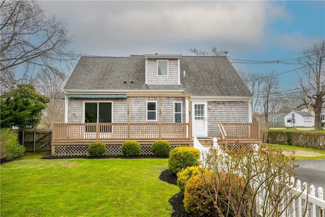 back of property with a yard, roof with shingles, fence, and a deck