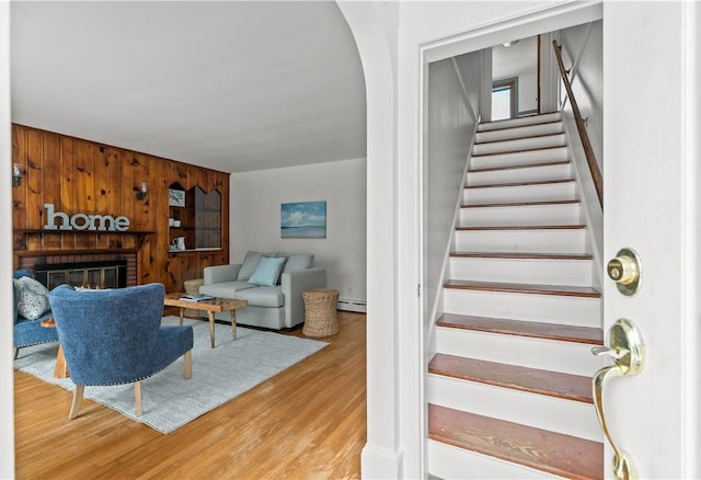 interior space with arched walkways, wood finished floors, a fireplace, and a baseboard radiator
