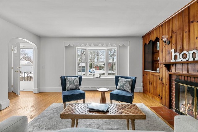 sitting room featuring arched walkways, light wood-style floors, a healthy amount of sunlight, and baseboard heating