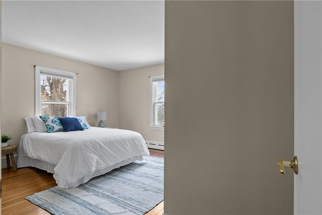 bedroom with a baseboard heating unit and light wood-style floors