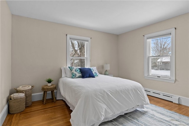 bedroom featuring a baseboard heating unit, wood finished floors, and baseboards