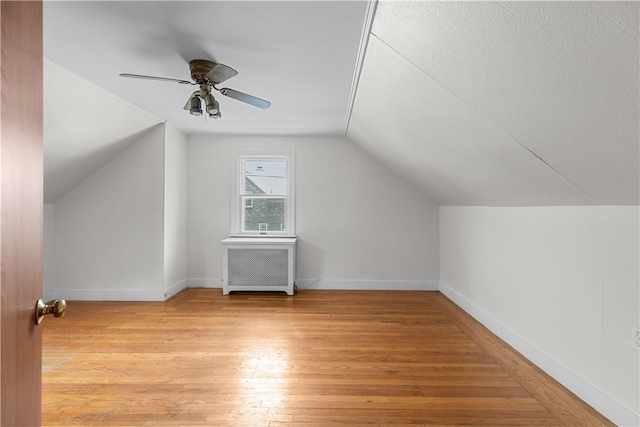 bonus room featuring light wood-type flooring, baseboards, radiator heating unit, lofted ceiling, and a ceiling fan