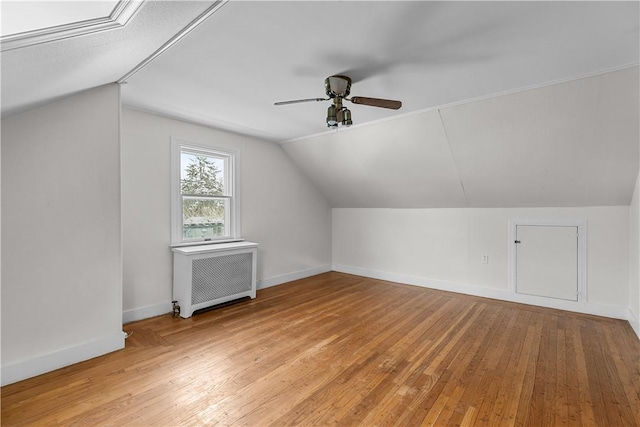 additional living space with radiator heating unit, light wood finished floors, vaulted ceiling, baseboards, and ceiling fan