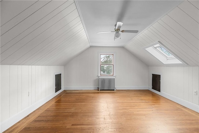 bonus room with a ceiling fan, radiator heating unit, lofted ceiling with skylight, and light wood finished floors
