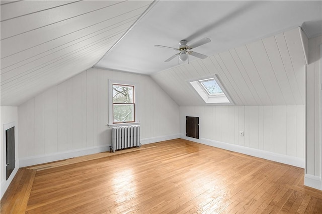 bonus room with light wood finished floors, vaulted ceiling with skylight, ceiling fan, and radiator
