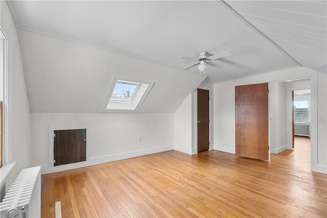 bonus room featuring radiator, a ceiling fan, lofted ceiling with skylight, baseboards, and light wood-style flooring