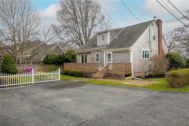 view of front of house with a shingled roof, a chimney, fence, and a deck