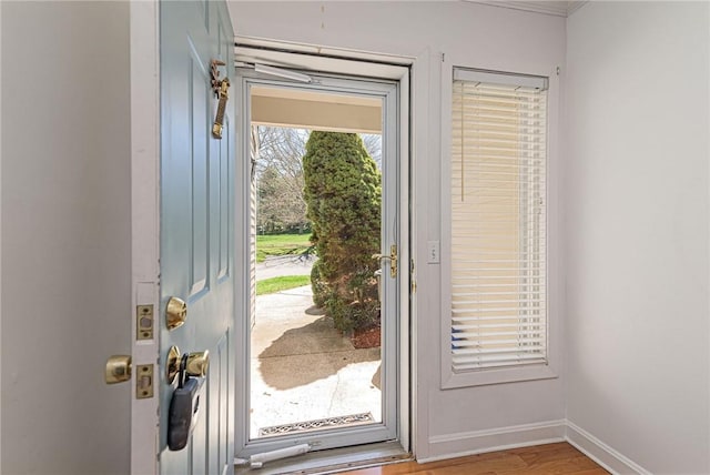 doorway with light wood-type flooring, baseboards, and ornamental molding
