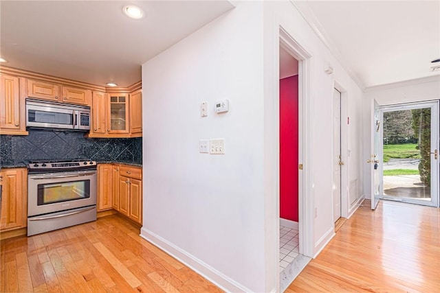 kitchen with decorative backsplash, glass insert cabinets, light wood finished floors, baseboards, and appliances with stainless steel finishes