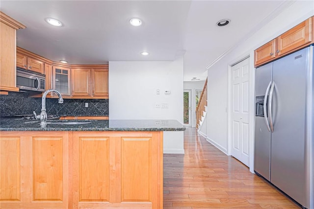 kitchen with stainless steel appliances, a sink, dark stone counters, decorative backsplash, and a peninsula