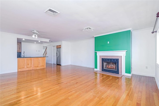 unfurnished living room with a ceiling fan, light wood-style flooring, a fireplace, baseboards, and visible vents