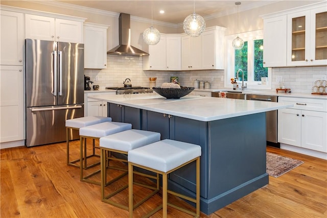 kitchen featuring wall chimney exhaust hood, a center island, appliances with stainless steel finishes, a breakfast bar area, and white cabinetry