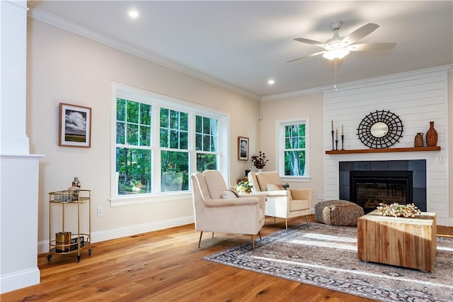 living room featuring baseboards, wood finished floors, a large fireplace, ceiling fan, and ornamental molding