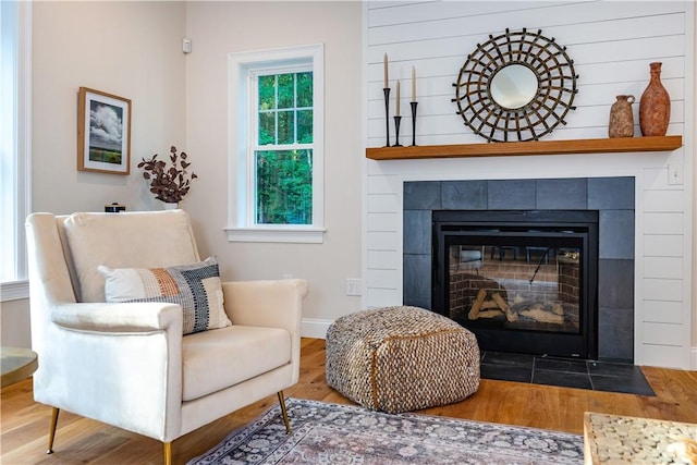living area with baseboards, a tile fireplace, and wood finished floors
