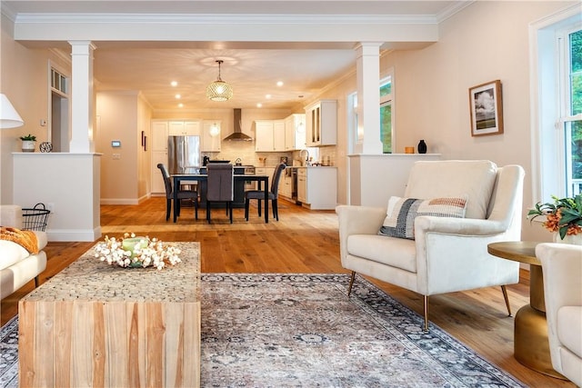 living area with ornamental molding, light wood finished floors, and decorative columns