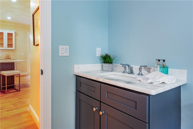 bathroom with tasteful backsplash, wood finished floors, crown molding, and vanity