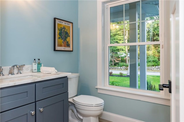 bathroom featuring baseboards, toilet, vanity, and a wealth of natural light