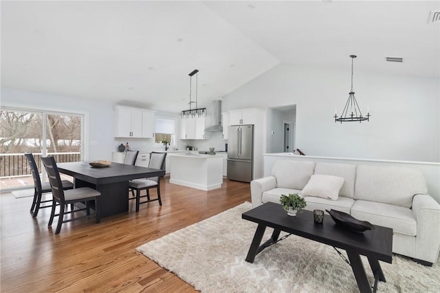 living area featuring light wood-style floors, vaulted ceiling, visible vents, and an inviting chandelier