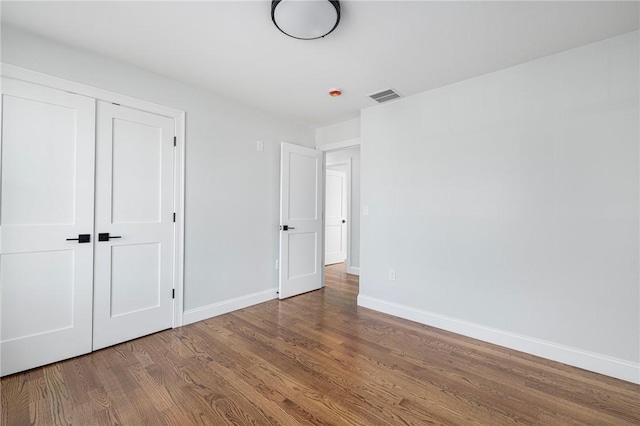 unfurnished bedroom with baseboards, wood finished floors, visible vents, and a closet
