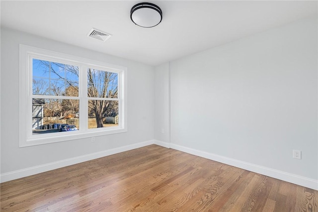 empty room featuring wood finished floors, visible vents, and baseboards