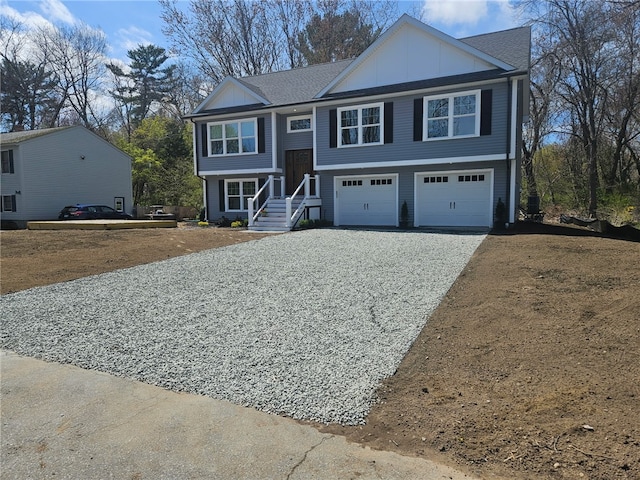 split foyer home with board and batten siding, an attached garage, and gravel driveway