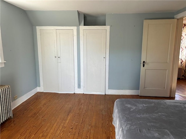 unfurnished bedroom featuring wood finished floors, baseboards, a closet, and radiator