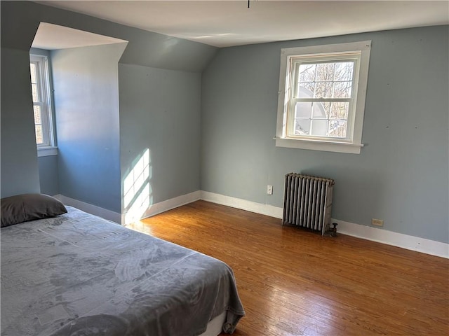 bedroom with multiple windows, lofted ceiling, radiator heating unit, and wood finished floors
