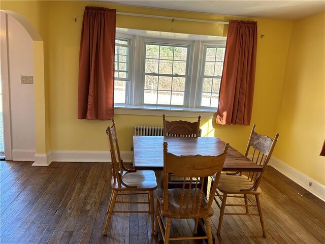 dining area with baseboards, arched walkways, dark wood-type flooring, and radiator