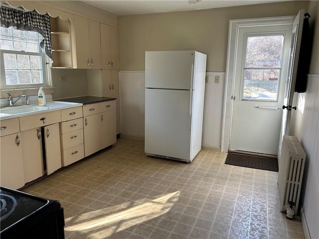 kitchen with radiator heating unit, cream cabinetry, light floors, a sink, and freestanding refrigerator