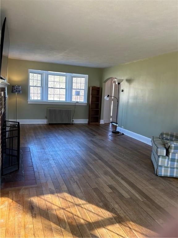 unfurnished living room with a fireplace, radiator heating unit, baseboards, and hardwood / wood-style flooring