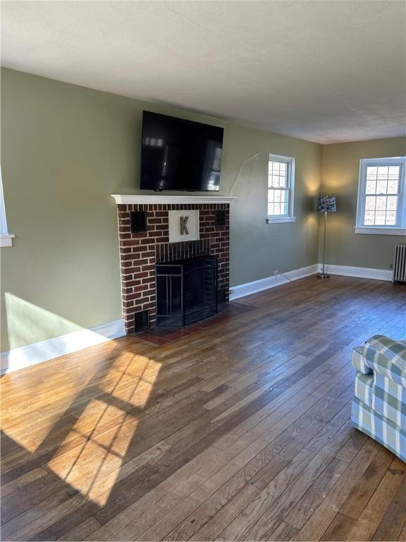 unfurnished living room with radiator heating unit, plenty of natural light, a fireplace, and wood-type flooring