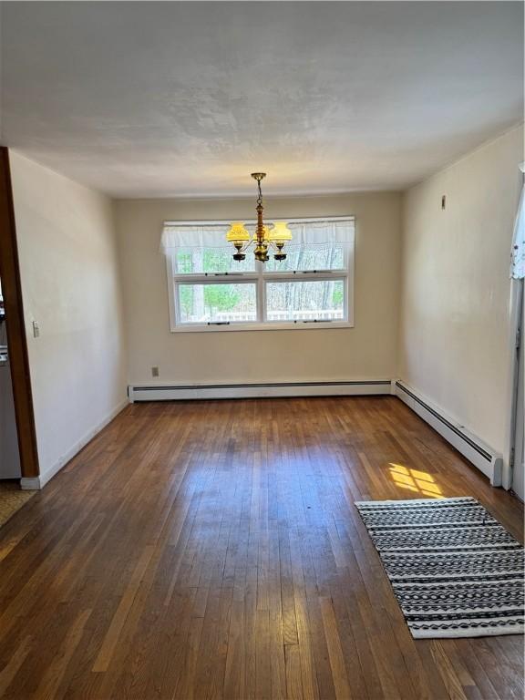 empty room featuring a healthy amount of sunlight, a baseboard radiator, hardwood / wood-style flooring, and a chandelier
