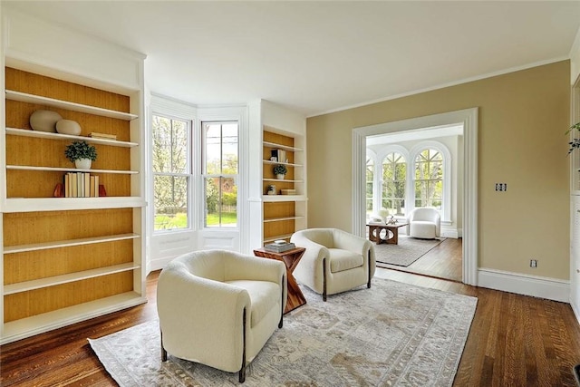 living area with wood finished floors, baseboards, ornamental molding, and built in shelves
