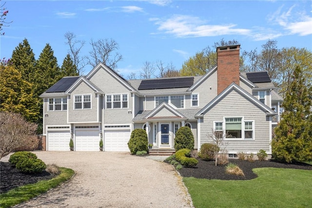 view of front of house featuring an attached garage, a chimney, aphalt driveway, and solar panels