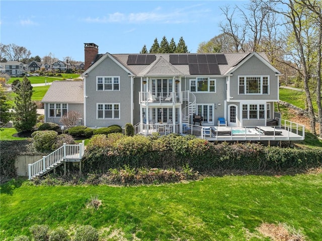 back of property with stairway, roof mounted solar panels, a chimney, a yard, and a wooden deck