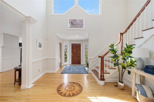 entrance foyer featuring stairway, a decorative wall, wainscoting, light wood-type flooring, and a towering ceiling