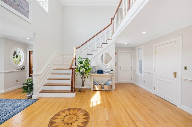 foyer with wood finished floors, a decorative wall, a towering ceiling, and stairs