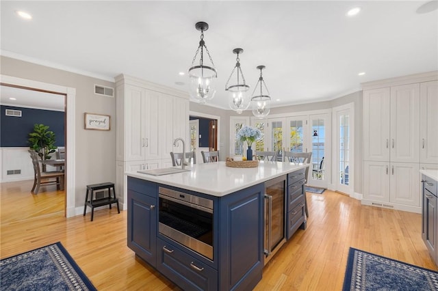 kitchen featuring light countertops, a sink, light wood-style flooring, blue cabinetry, and a notable chandelier