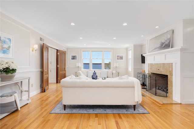 living area with light wood-type flooring, a tiled fireplace, visible vents, recessed lighting, and ornamental molding