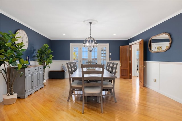dining area with light wood finished floors, a wainscoted wall, an inviting chandelier, and ornamental molding