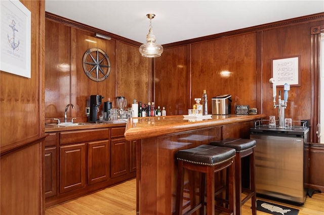 bar featuring a sink, wet bar, light wood-style floors, wood walls, and hanging light fixtures